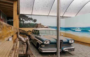 Classic car parked with a painted beach mural behind.