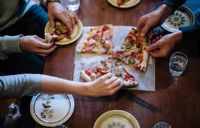 Hands reaching for slices of a pizza in the middle of the table at Mamma Mia.