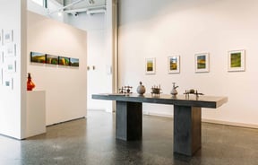 A bold table displaying art, sitting in front of white walls filled with art.