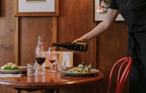 A bottle of red wine being poured into a wine glass on a table.