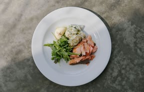 A white plate with potato salad, salmon and a green salad on the side.