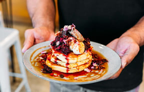 Man holding a plate of hotcakes with berries from t bay cafe, Porirua.