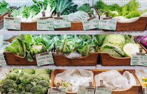 A full shelf of green vegetables in wooden boxes.