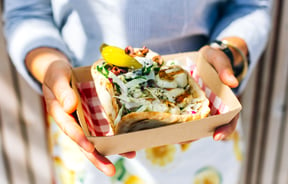 A souvlaki in a cardboard container in the hands of a customer.