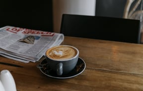 Close up of a flat white and newspaper on a table.