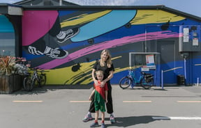 A woman and her son standing in front of a colourful mural painted on the exterior of a building.