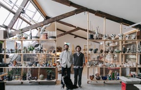 Jamie Smith and Tom Baker of Kiln Studio standing in their studio with a black dog.