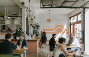 Customers sitting at tables inside a sunny cafe.