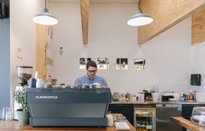 Man making coffee behind blue coffee machine at Dispense Espresso in Christchurch.