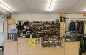 A man working behind the counter at Embassy where lots of caps are displayed on shelves.