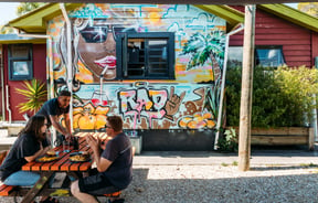 Customers sitting at a picnic table outside Roots Bar on a sunny day.