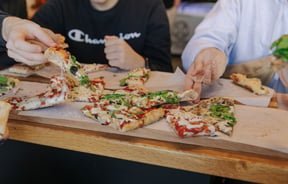 People sitting around a table with a pizza in the middle all sharing.