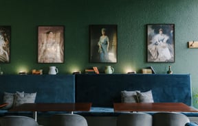 Plush blue seating set against a dark green wall filled with portraits of queens