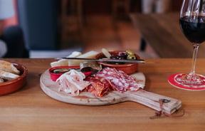 A glass of red wine next to a platter of cheese and cured meats at Salut Salut.