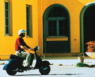 Man on vespa in front of yellow building in Italy