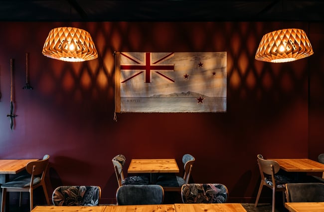 An old New Zealand flag on a red wall above tables and chairs.