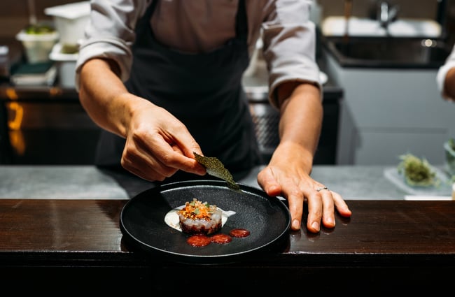 A chef placing dried seaweed on a dish.