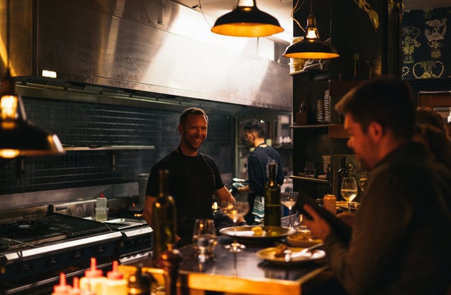 Chef in the kitchen smiling at patrons across the bar at 5th Street restaurant Christchurch.