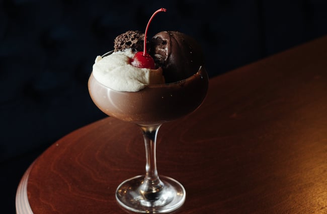 Close up of a chocolate-coloured cocktail with cream and a cherry on top on a wooden table at 5th Street restaurant Christchurch.