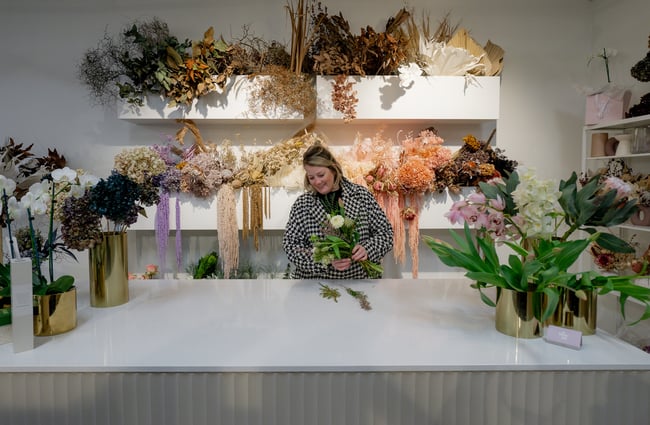 A woman smiling behind a counter holding a bouquet of flowers.