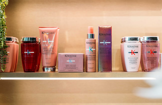 A close up of pink Kerastase hair products on a brightly lit shelf.