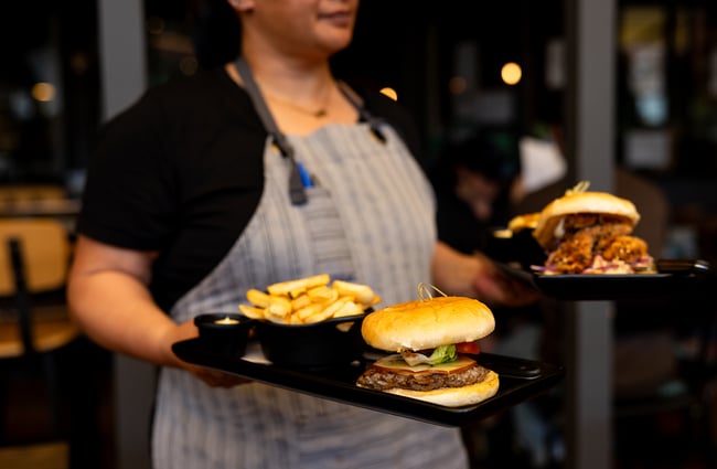 A staff member holds two plates of burgers and fries.