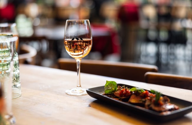 A glass of wine and small meat dish sit on a table at Atticus Finch.