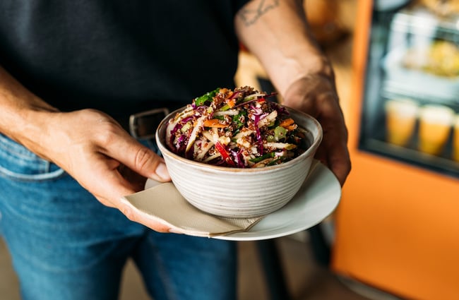 A person holding a colourful salad in a bowl.