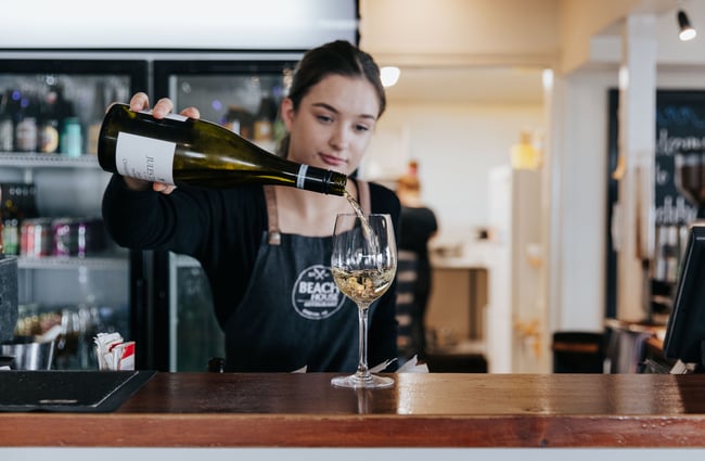 A woman pouring a glass of wine behind the bar.