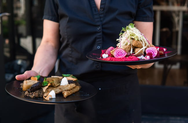 Waitstaff in black uniform holding two plates of colourful food at Bonobo, Christchurch.