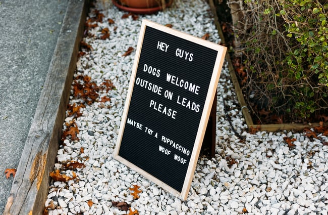 A black and white sign promoting dogs on leads at the cafe.
