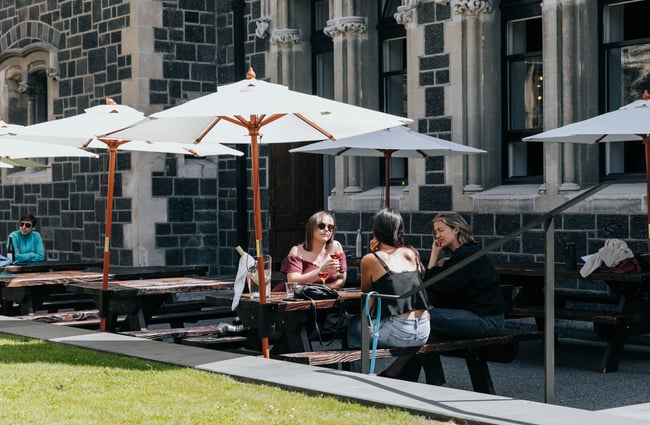 Three people drinking wine at an outdoor table under an umbrella at Cellar Door in Christchurch.
