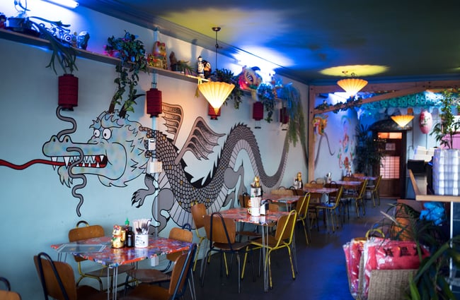 Dragon artwork on a blue wall behind dine in tables.