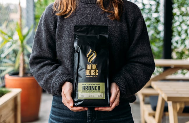 A woman wearing a grey jumper holding a bag of Dark Horse coffee beans.