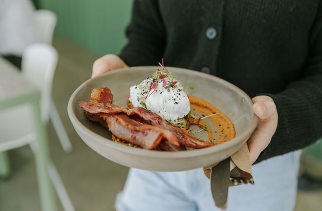 A wait staff holding bacon and poached eggs on a plate.