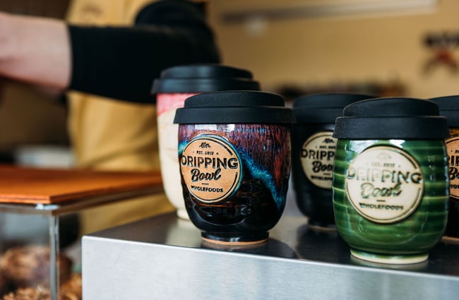 Counter display of colourfully glazed ceramic takeaway cups with Dripping Bowl's logo embossed on the front.
