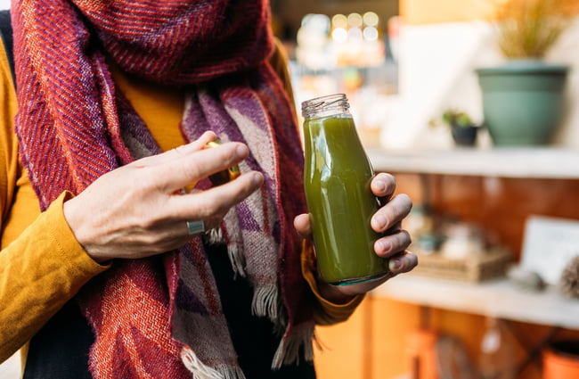A person holds a small glass bottle of green juice.