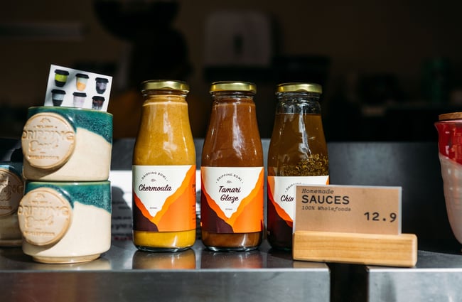 Homemade Dripping Bowl sauces and ceramic mugs for sale on the counter at Dripping Bowl.