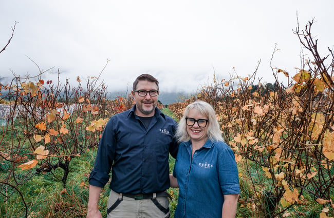 A man and woman smiling to camera in a vineyard on an autumn day.
