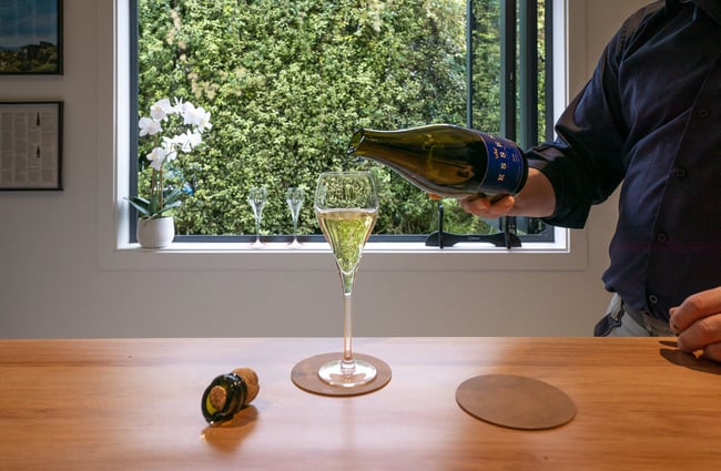 A bottle of wine being poured into a champagne glass.