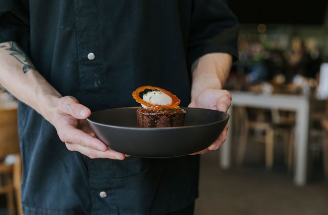 A chef in a black jacket holding a bowl with a dessert.