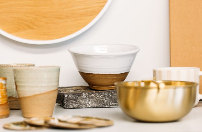Neutral coloured ceramics or cups and bowls on display on a white shelf.