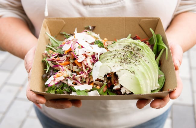 Close image of a person holding a cardboard takeaway dish of a salad with avocado at Herba Gourmet in Christchurch.