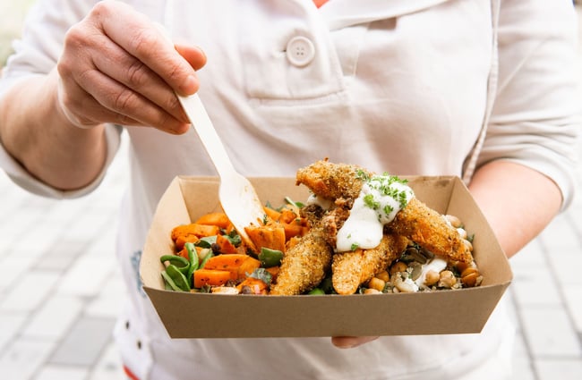 Person holding a cardboard takeaway dish of mixed salads and crumbed fillets and at Herba Gourmet in Christchurch.