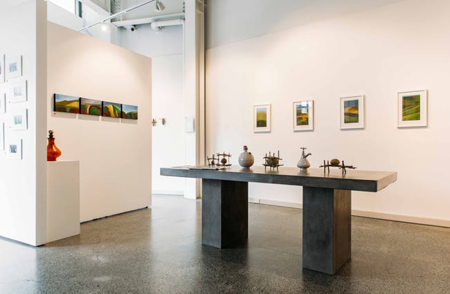 A bold table displaying art, sitting in front of white walls filled with art.