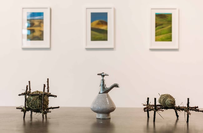 Three sculptures sitting on a table with art work displayed on a white wall in the background.