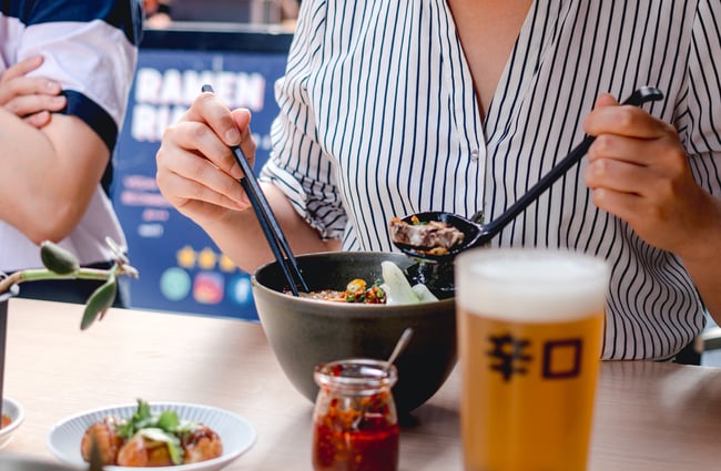 Woman eating a bowl of ramen with pint of beer.