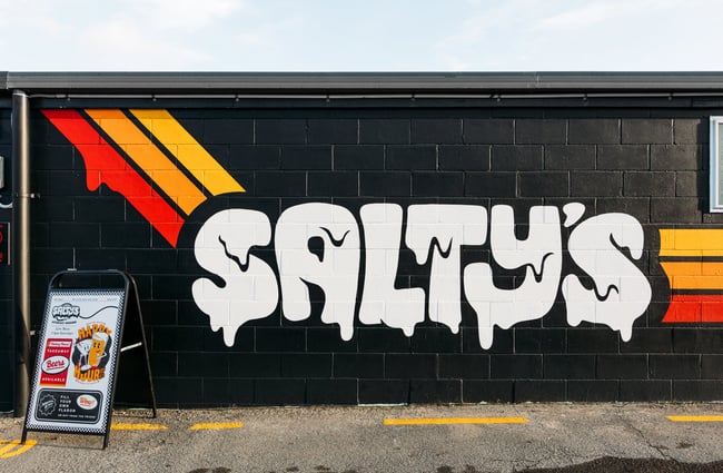 A white 'Salty's sign' painted on a black wall.