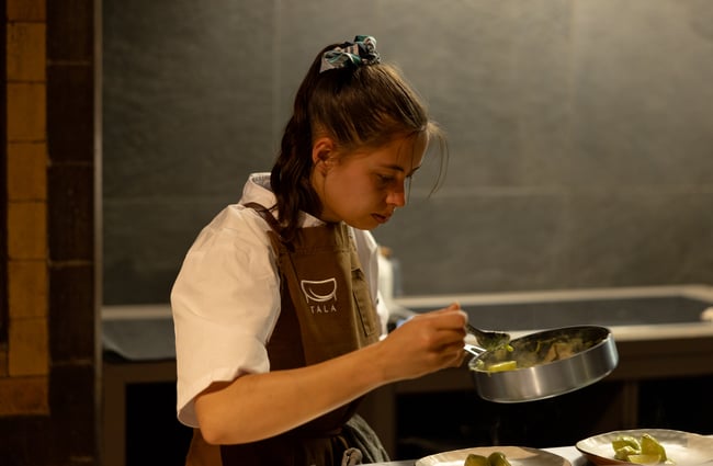 A female chef looking into a pot.