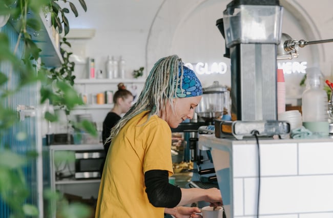 A barista wearing a yellow top making a coffee.